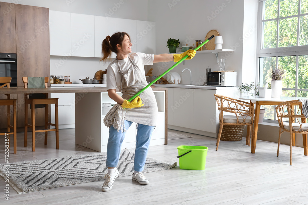 Pretty young woman having fun with mop in modern kitchen - obrazy, fototapety, plakaty 