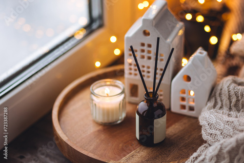 Aroma diffuser, burning candle, Christmas perfume on wooden bamboo tray, knitted sweater. Cozy home decor, hygge and aromatherapy concept. Comfortable atmosphere, Scandinavian decor.
