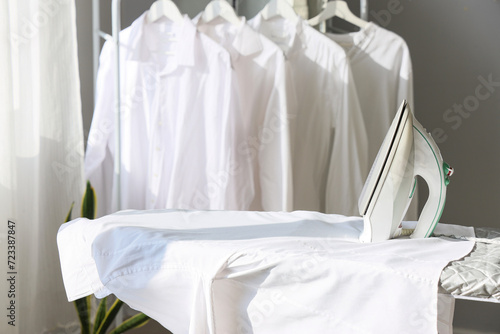 Electric iron with white shirt on board in room