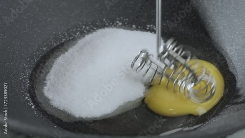 Cooking process. Preparation of the dough. Dark gray bowl with sugar and raw egg. The cook beats the egg with the sugar with a metal whisk. photo