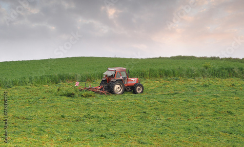 Farm tractor doing grass cutting work in a field at the end of a rainy and sunny day