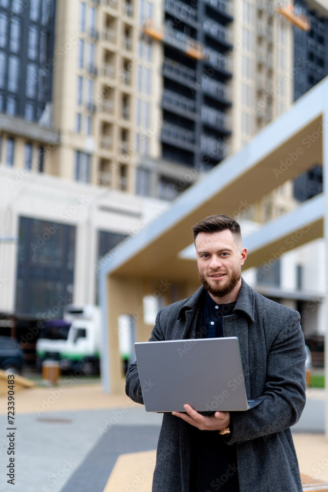Man stands on the background of new building and holds laptop in his hands Man stands on the background of new building and holds laptop in his hands