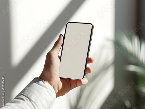 Close-up of a smartphone mockup held in one hand against a white wall with candela shadows and sunlight from outside. Created with Generative AI.