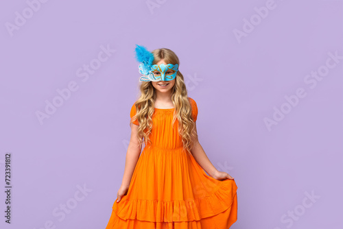 Happy little girl wearing carnival mask on lilac background