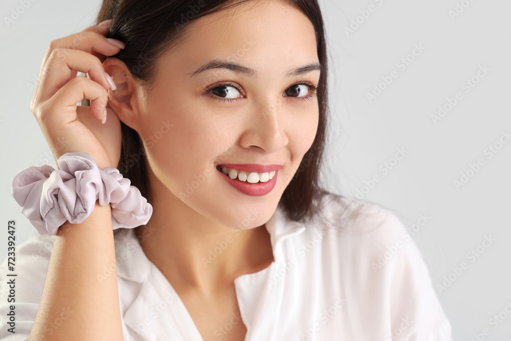 Young Asian woman with scrunchy on light grey background, closeup