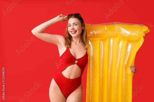 Beautiful young woman in tank swimsuit and with inflatable mattress on red background © Pixel-Shot