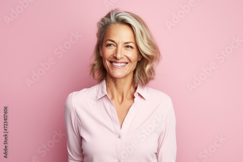 Portrait of smiling senior woman in pink shirt over pink background