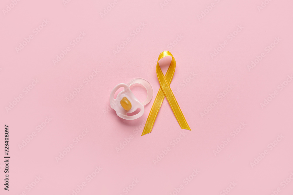 Golden ribbon with pacifiers on pink background. Childhood cancer awareness concept Golden ribbon with pacifiers on pink background. Childhood cancer awareness concept
