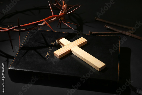 Wooden cross with crown of thorns, Bible and nails on black background. Good Friday concept