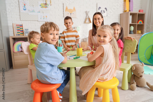Bild auf Leinwand Little children with nursery teacher drawing at table in kindergarten