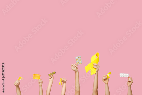 Children hands holding pills and yellow ribbons on pink background. International Childhood Cancer Day © Pixel-Shot