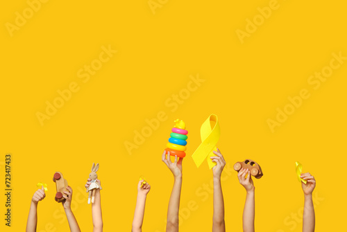 Children hands holding toys and yellow ribbons on color background. International Childhood Cancer Day