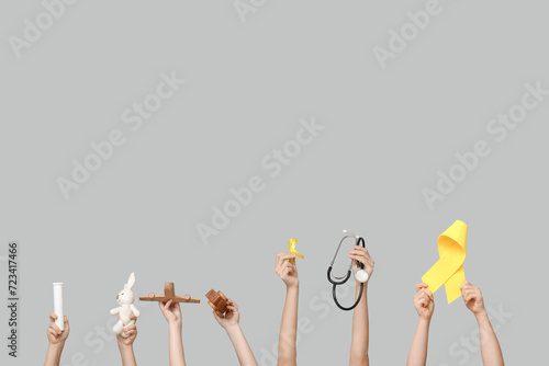 Children hands holding toys, stethoscope and yellow ribbons on grey background. International Childhood Cancer Day
