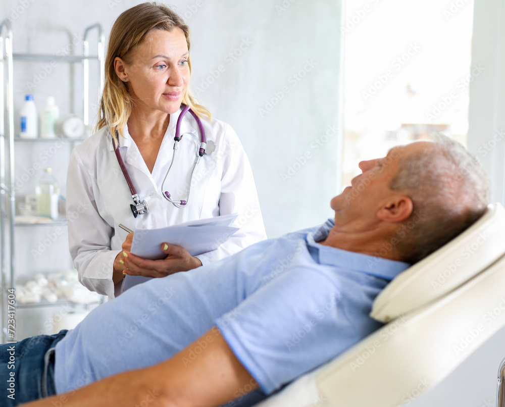 Fototapeta premium Adult woman medic makes notes in documents in medical room