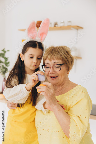 Happy grandmother and granddaughter in easter bunny ears having egg tapping with easter eggs