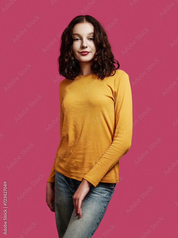 Yong teenager girl simple pose. Rich saturated red color background. Model or influencer studio shot. Beauty and fashion. Slim body type and calm face expression. Wearing yellow long sleeve shirt. Yong teenager girl simple pose. Rich saturated red color background. Model or influencer studio shot. Beauty and fashion. Slim body type and calm face expression. Wearing yellow long sleeve shirt.