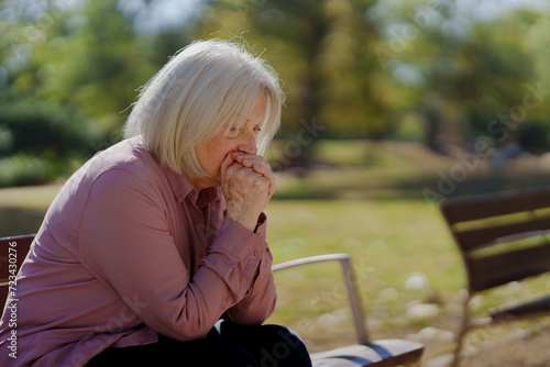 Worried senior woman thinking in a park. Sad elderly person suffering depression.