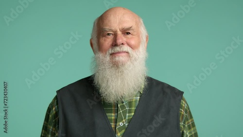 An agreeable elderly man in a checkered shirt and vest nods his head in a gesture of approval or affirmation, against a soothing turquoise background. Camera 8K RAW.  photo