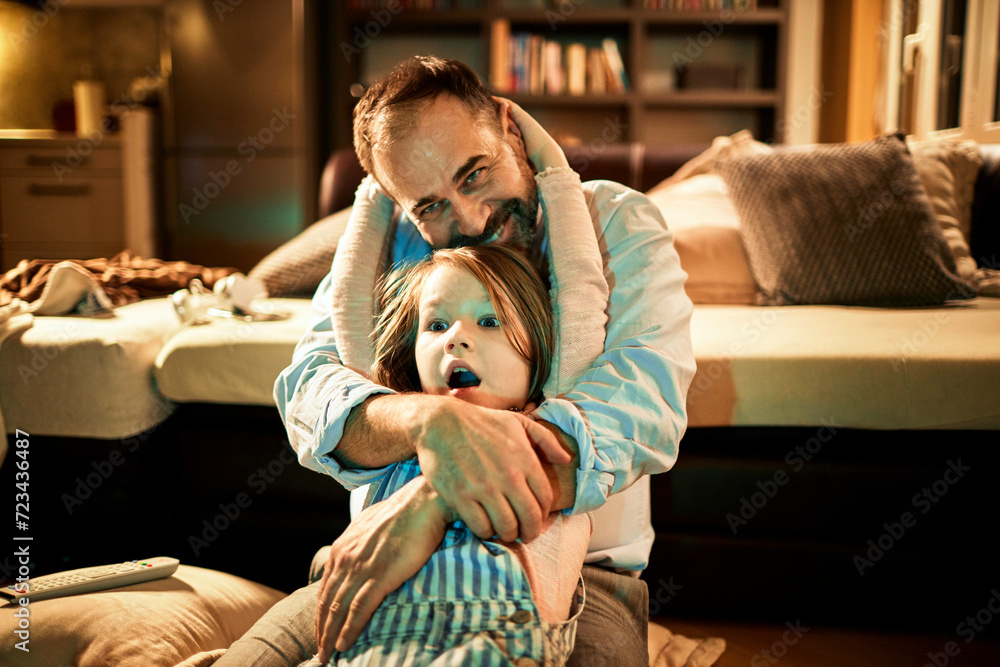Father and daughter watching tv in the living room at home and eating popcorn