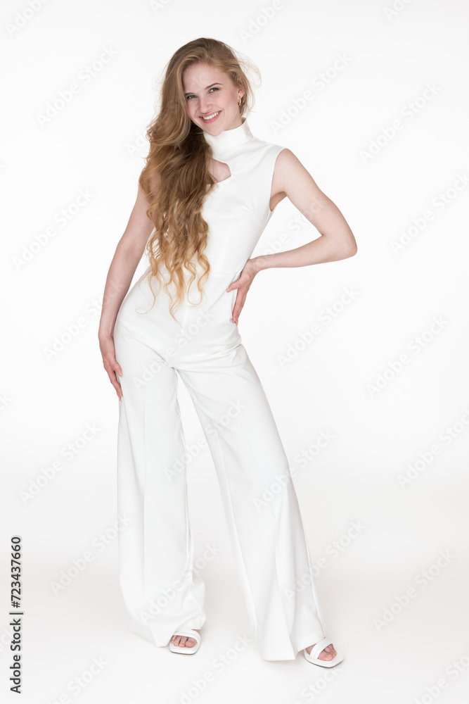 Happiness young woman stylishly dressed in white long jumpsuit straight design standing in full length. Caucasian woman with long blonde hair looking at camera. Studio shot on white background