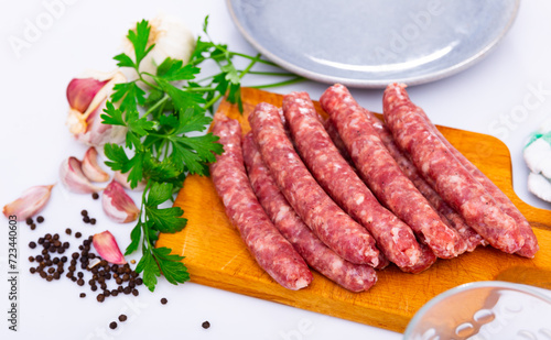 Raw spicy longaniza sausages from minced pork prepared for frying lying on wooden board with knife, garlic, peppercorns and fresh parsley. Traditional Spanish specialty..