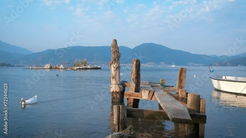 Wooden handmade pier in sun. A view of sunny day with wooden handmade pier and fishing baot in lake water against mountains in summer. photo