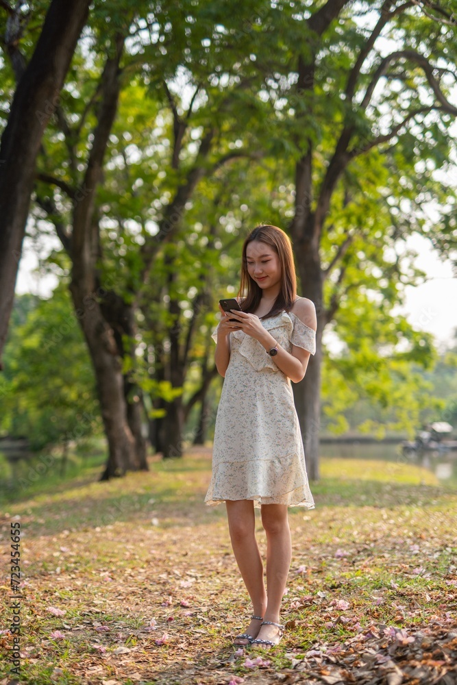 Beautiful woman using phone in a greenery park during sunset Beautiful woman using phone in a greenery park during sunset