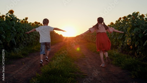 Children boy girl playing together in nature. Brother, sister fantasize about flying into sunset. Cheerful children play, run with their hands raised in field of sunflowers in summer, dream of flying.