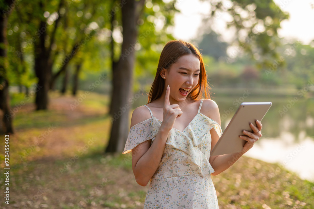 Beautiful Young Asian Woman Finds Serenity, Nature, and Inspiration While Holding a Digital Tablet in the Sunset Breeze at the Park Beautiful Young Asian Woman Finds Serenity, Nature, and Inspiration While Holding a Digital Tablet in the Sunset Breeze at the Park