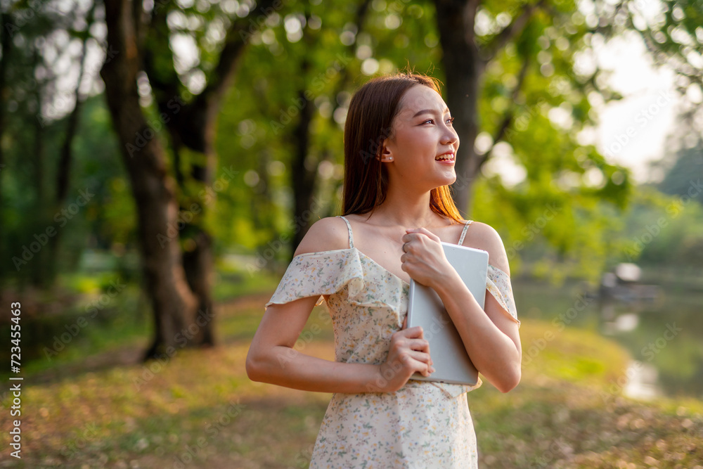 Beautiful Young Asian Woman Finds Serenity, Nature, and Inspiration While Holding a Digital Tablet in the Sunset Breeze at the Park Beautiful Young Asian Woman Finds Serenity, Nature, and Inspiration While Holding a Digital Tablet in the Sunset Breeze at the Park