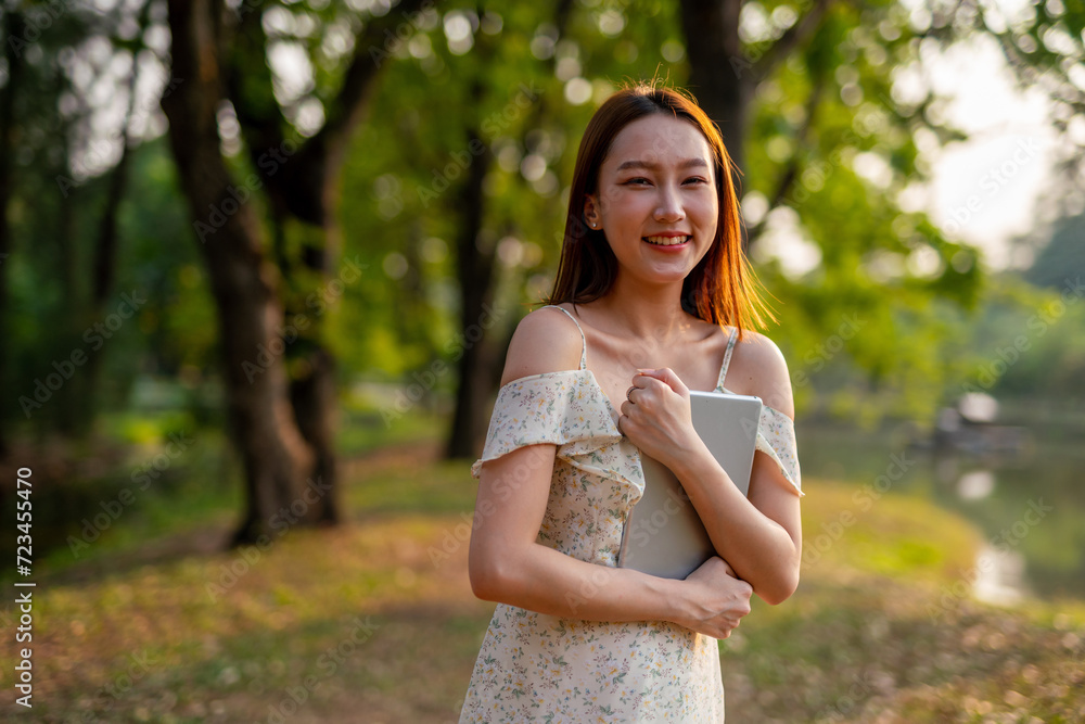 Beautiful Young Asian Woman Finds Serenity, Nature, and Inspiration While Holding a Digital Tablet in the Sunset Breeze at the Park Beautiful Young Asian Woman Finds Serenity, Nature, and Inspiration While Holding a Digital Tablet in the Sunset Breeze at the Park