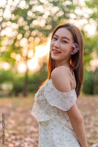 Young Asian beauty enjoys playing and posing with sakura flowers at a public park during sunset moments