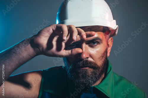 Closeup portrait of tired builder in construction helmet. Fatigued worker wipes sweat from forehead. Hard work at construction site. Heavy profession. Handsome male architect or engineer in hard hat. photo