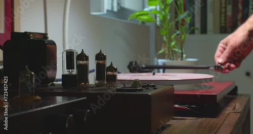 Camera on slider smoothly pushing past tube amplifier to turntable with man placing a stylus on pink colored vinyl record.