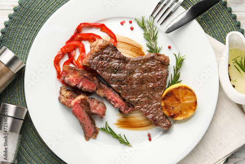 Delicious grilled beef steak with pepper, spices and lemon served on table, flat lay