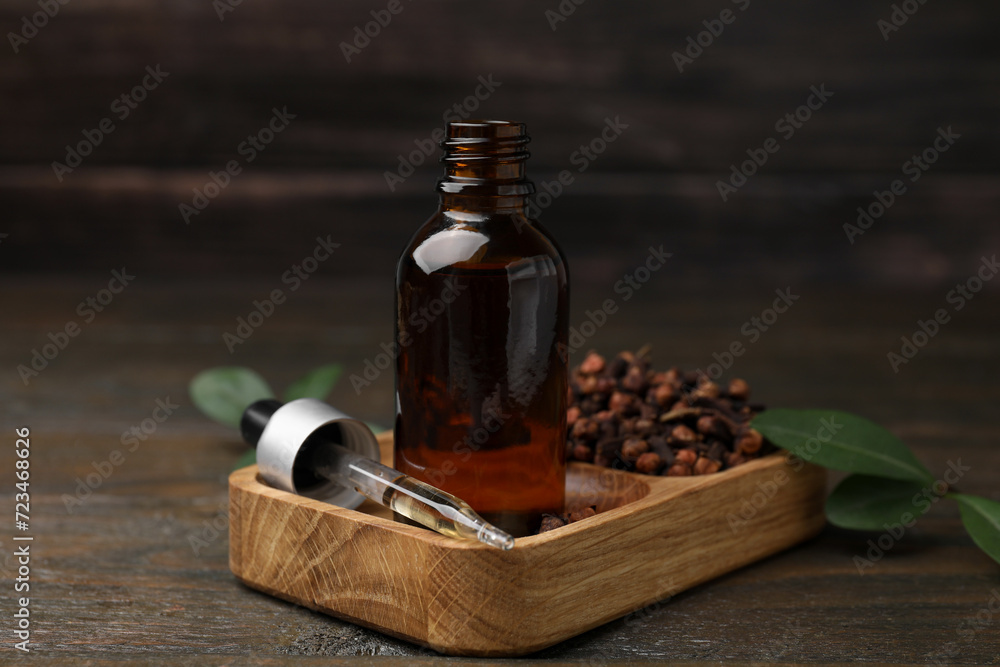 Clove oil in bottle, pipette and dried buds on wooden table, closeup Clove oil in bottle, pipette and dried buds on wooden table, closeup