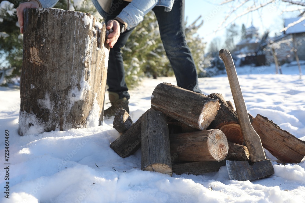 Man preparing stump for chopping outdoors, closeup. Axe and pile of logs on snow, selective focus Man preparing stump for chopping outdoors, closeup. Axe and pile of logs on snow, selective focus