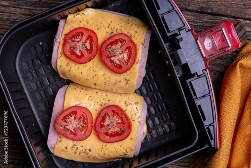 Two slices of lache bread with slices of tomato, cheddar cheese and ham inside the airfryer seen from above on a rustic wooden table with selective focus
 photo