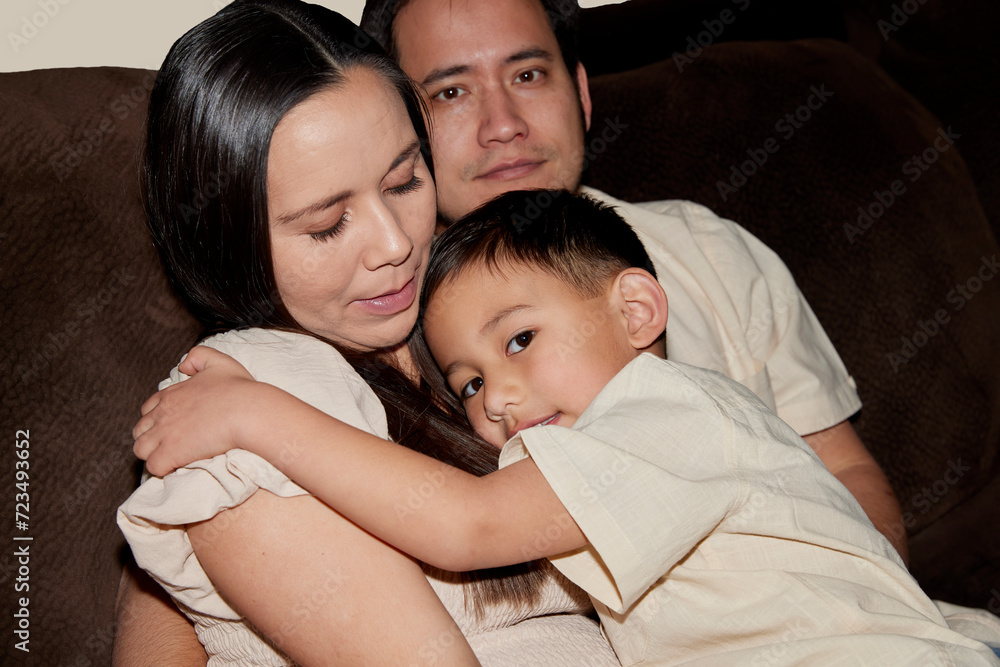 A young married couple sitting next to each other with their son on a brown couch A young married couple sitting next to each other with their son on a brown couch