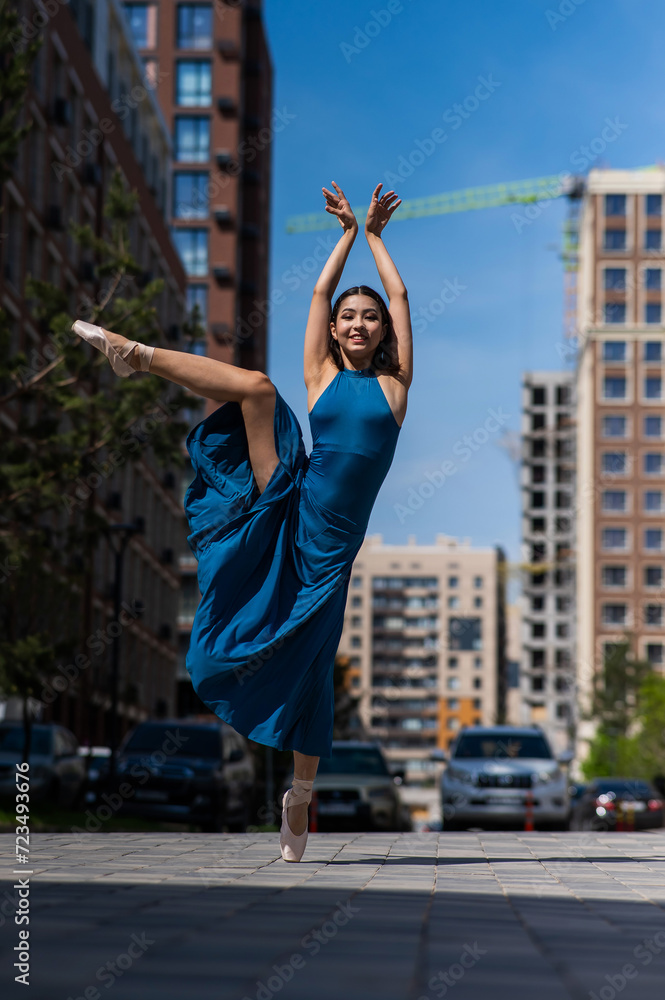 Beautiful Asian ballerina in blue dress posing in splits outdoors. Urban landscape. Vertical photo. 