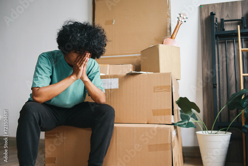 Tired unhappy Asian man moving out from apartment. Sad evicted man worried relocating house  photo