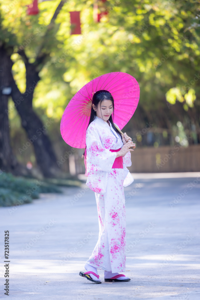 Asian woman wearing japanese traditional kimono. Beautiful Woman smiling, holding a umbrella walking outside. Woman in Kimono dress enjoying and walking on street outdoors in slow motion.