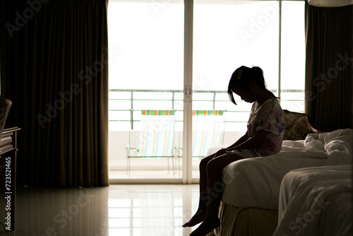 silhouette of a sad little girl sitting in bed at home, family problems. fear and fobies of child. Psychological portrait of scared young girl.