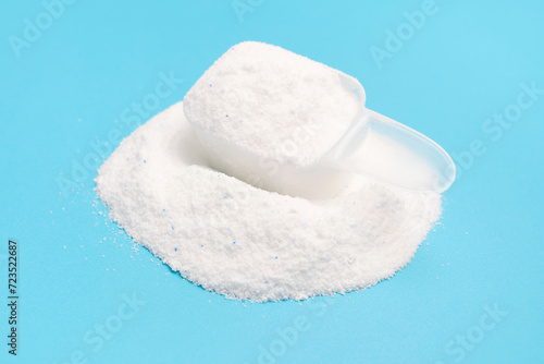 Washing powder in a measuring spoon on blue background side view close-up.