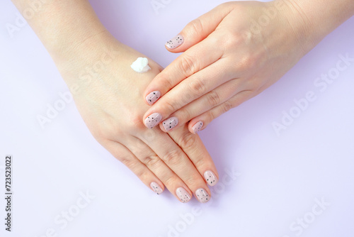 Woman applying moisturizer to her hands close-up, top view on lilac background.