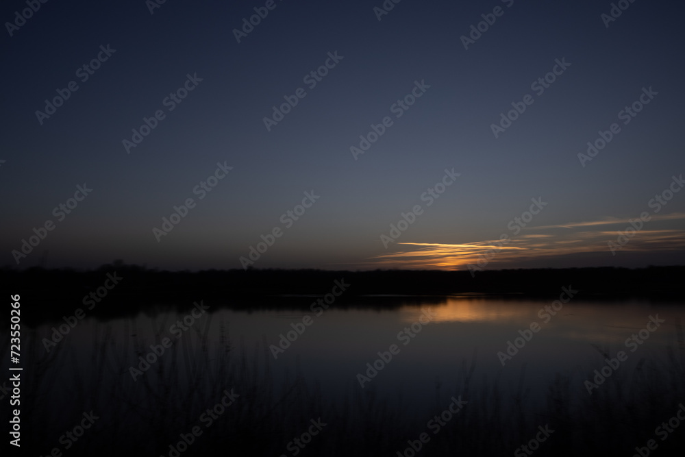 Obraz premium This image offers a minimalist view of dusk's final moments, where the last streaks of sunlight cast a subdued glow on the horizon. The sky transitions from the warm tones of the fading sun to the