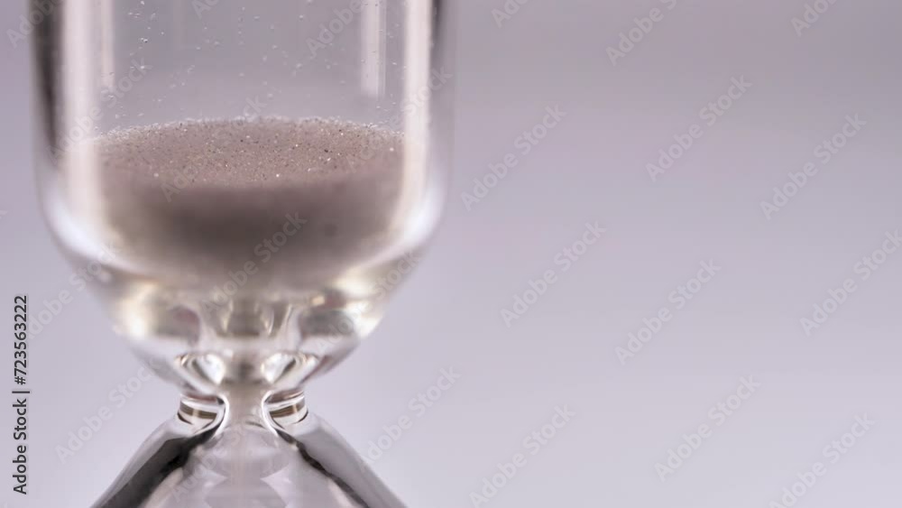 White sand running in an hourglass. Macro shot with selective focus on light background with copyspace. White sand running in an hourglass. Macro shot with selective focus on light background with copyspace.