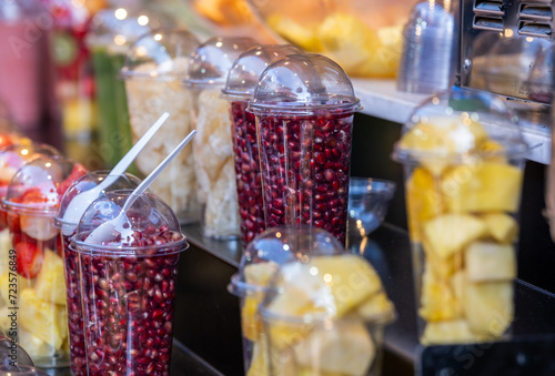 Fresh pomegranate seeds and pineapple pieces in plastic transparent cups for sale at the farmers market photo