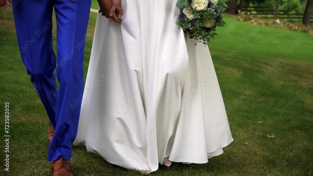 Closeup shot of the legs of bride and groom walking together on the grass in the park on the sunny wedding day Closeup shot of the legs of bride and groom walking together on the grass in the park on the sunny wedding day