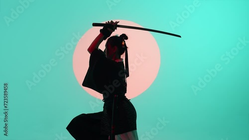 Young asian woman in a traditional kimono removing the katana from the sheath in militant pose in the studio with a turquoise blue green background and red sun photo